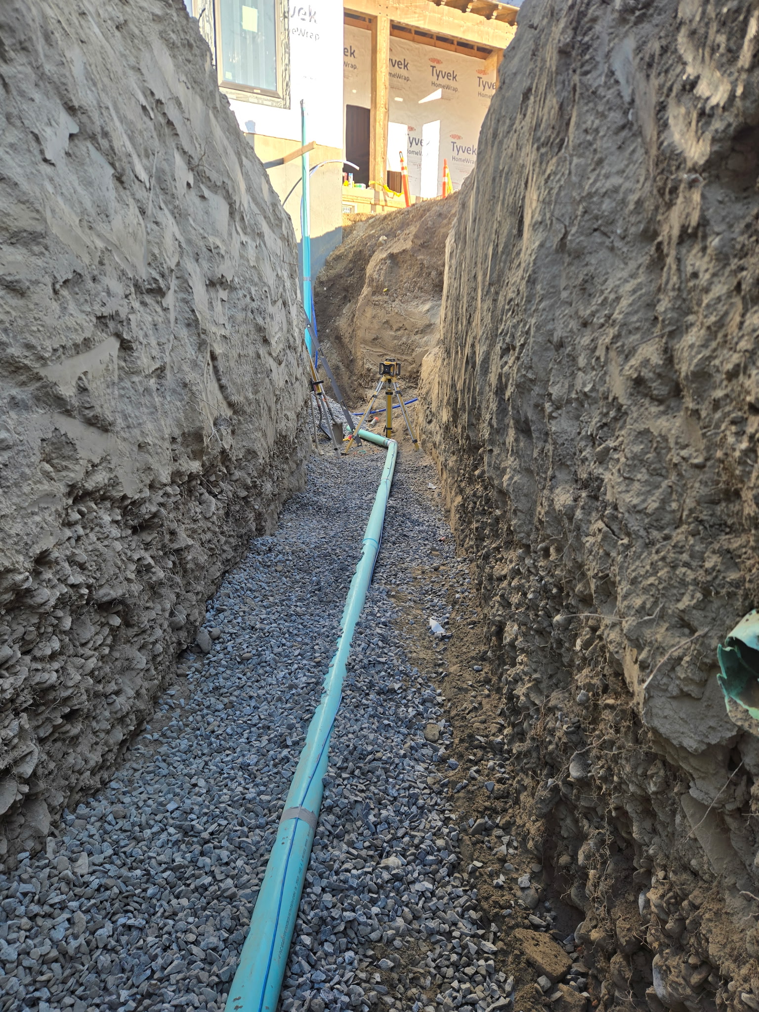 Deep trench with blue sewer pipe on gravel bed
