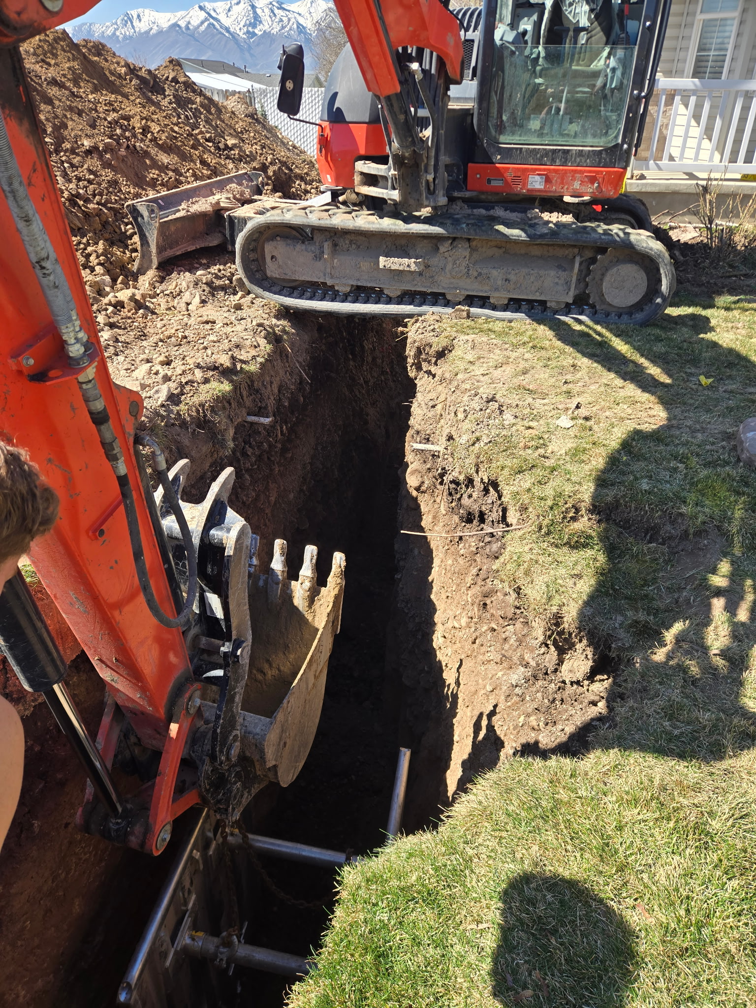 Excavator digging deep trench next to residential home