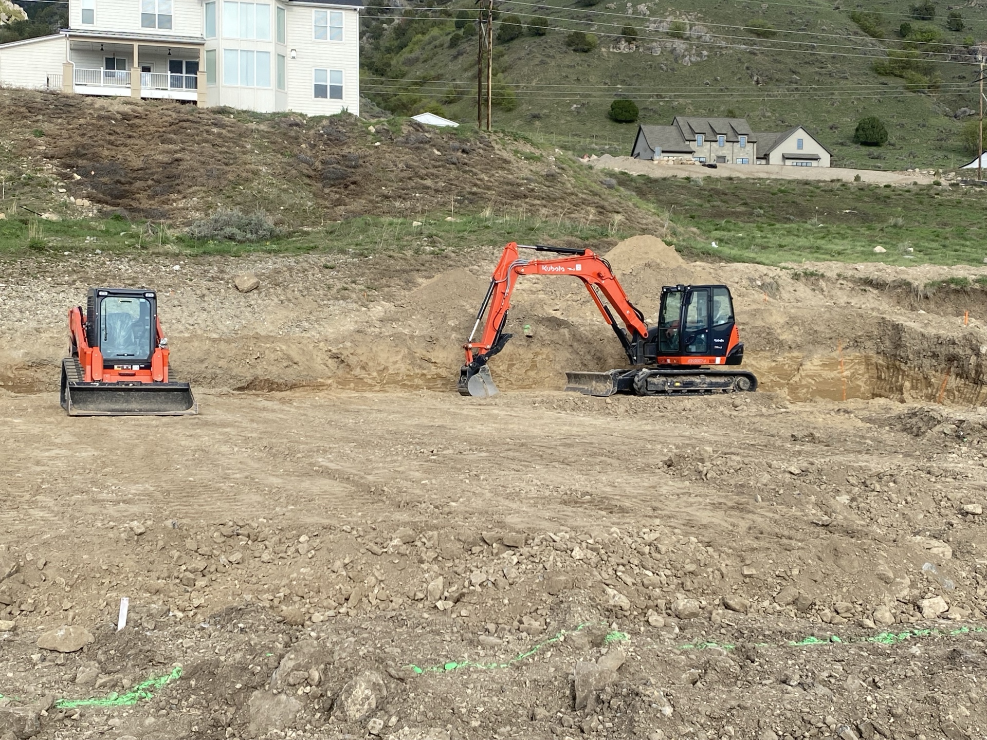 Two machines grading a large site with mountain backdrop